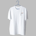 Charger l'image dans la visionneuse de la galerie, A white t-shirt on a blue wire hanger against a light grey background. It features a small embroidered design on the left chest depicting a simple black line-art figure lifting an orange barbell over their head.
