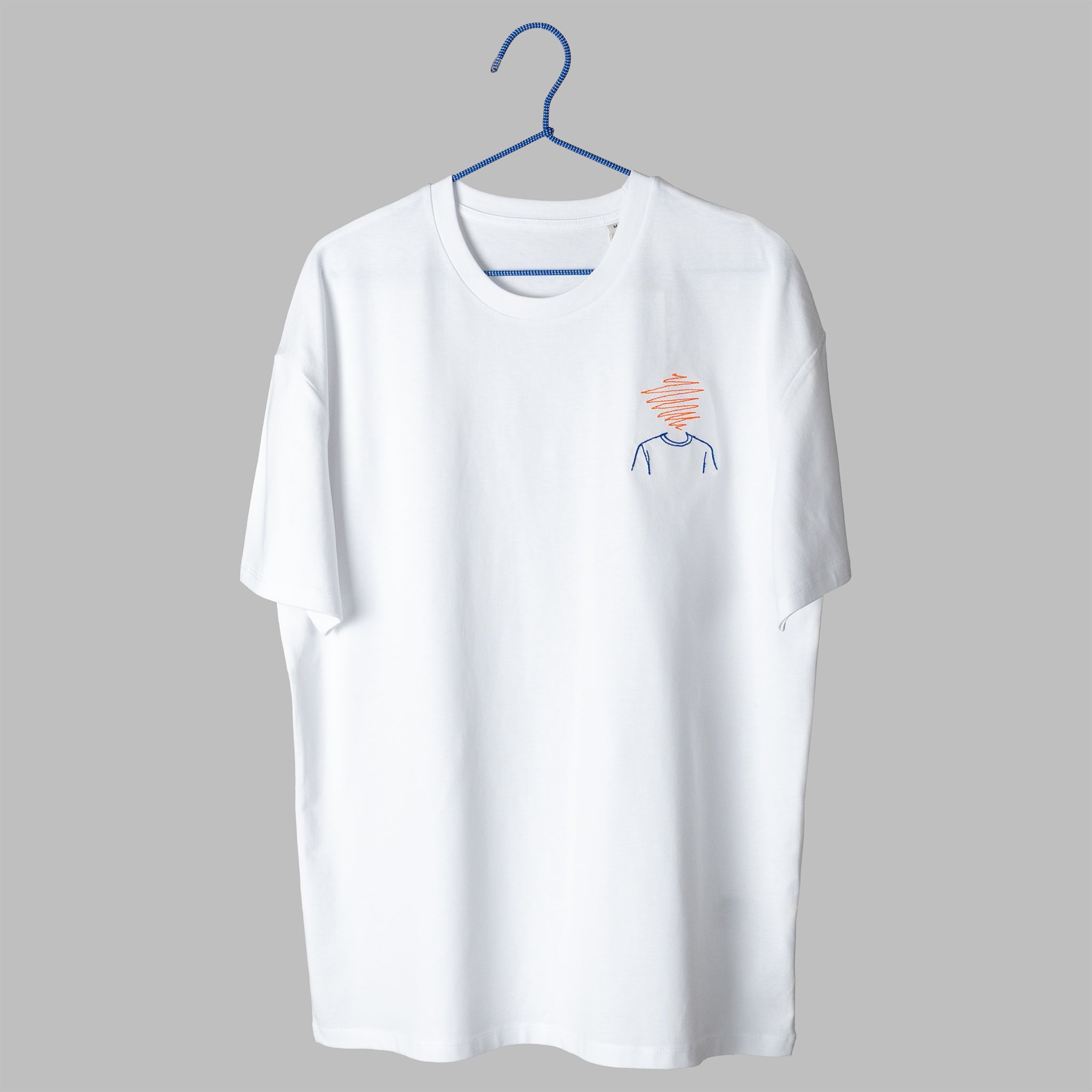 : A white t-shirt on a blue wire hanger against a light grey background. It features a small embroidered design on the left chest depicting the blue outline of a person's shoulders and neck, with a tangled orange scribble where the head should be.