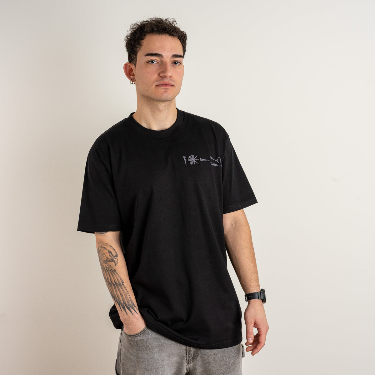 Model wearing Gordina’s Undeciphered black T-shirt, showing the small embroidered chest motif.