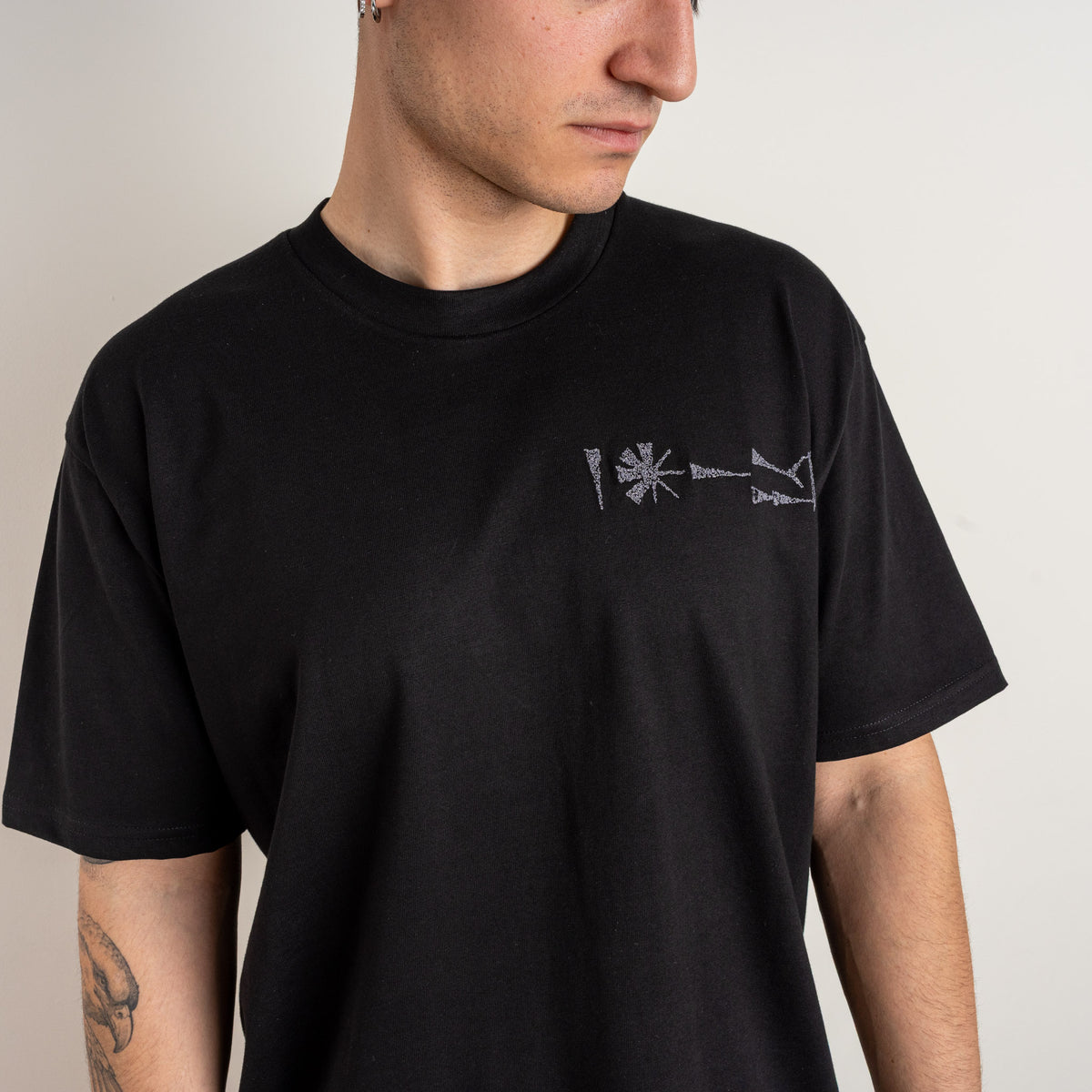Back view of a model wearing the plain-back Gordina Undeciphered black T-shirt.
