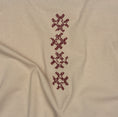 Load image into Gallery viewer, Angled close-up of burgundy cross-stitch embroidery on the beige Gordina Unsigned T-shirt.
