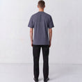 Load image into Gallery viewer, Back view of a model wearing the Gordina Unsigned faded indigo T-shirt with vertical navy cross embroidery.
