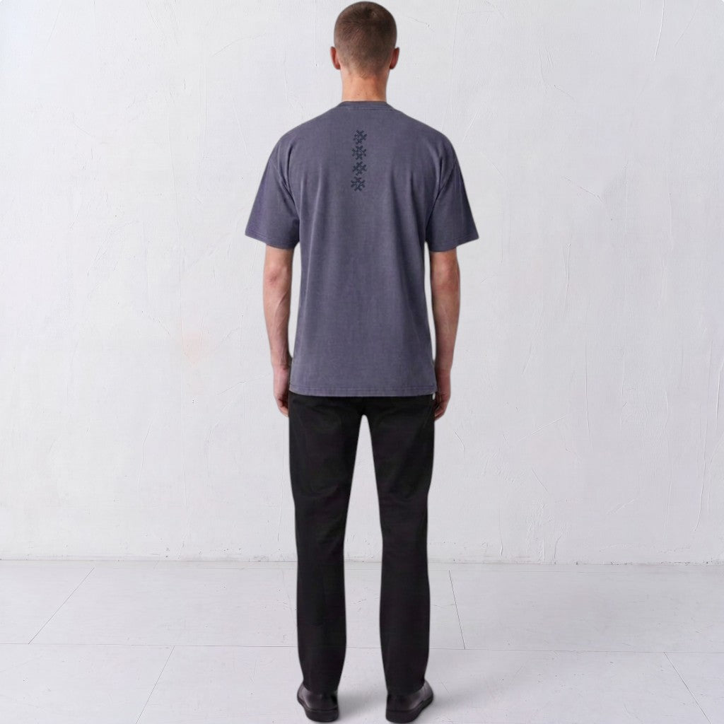 Back view of a model wearing the Gordina Unsigned faded indigo T-shirt with vertical navy cross embroidery.