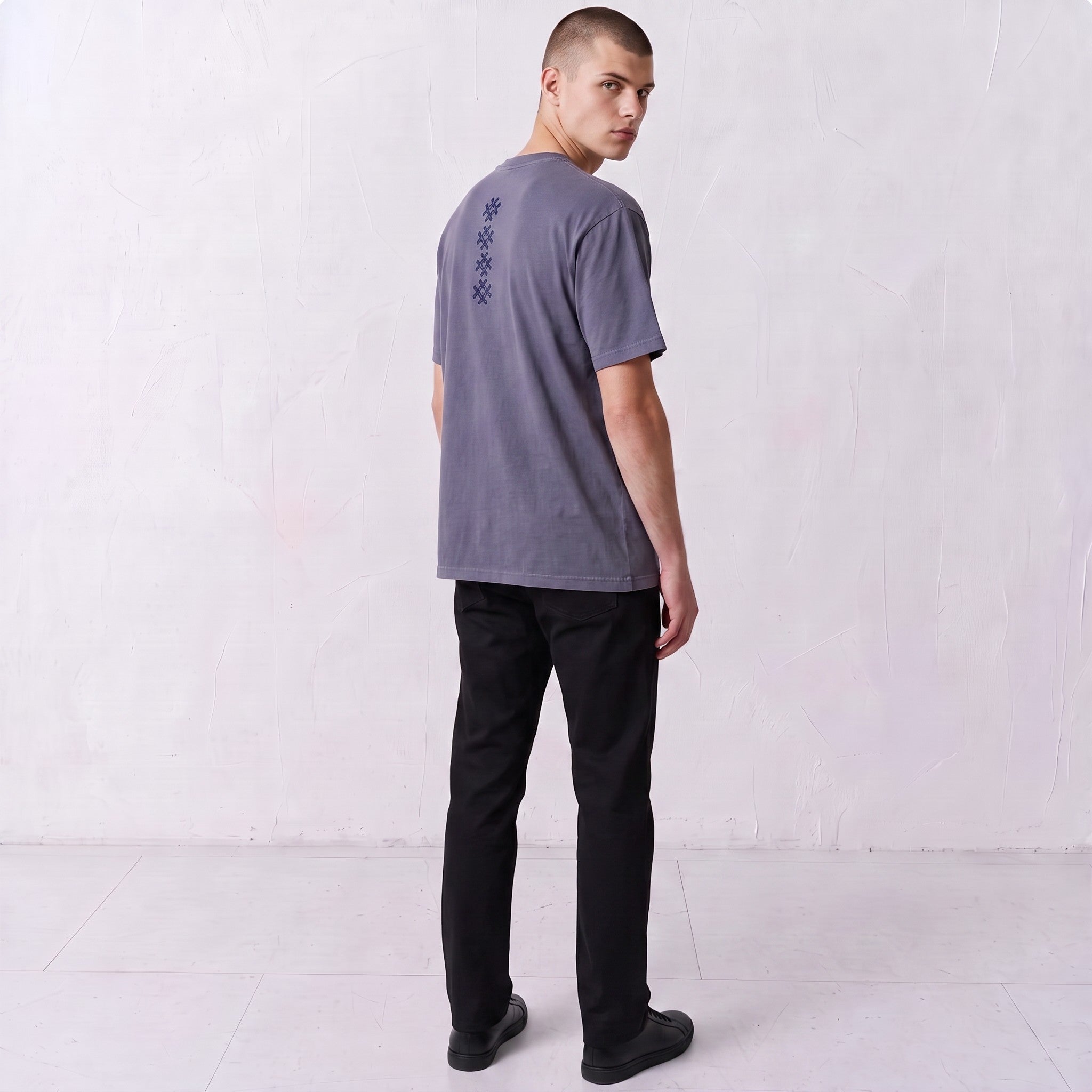 Three-quarter back view of a model wearing the Gordina Unsigned faded indigo T-shirt with navy cross embroidery.
