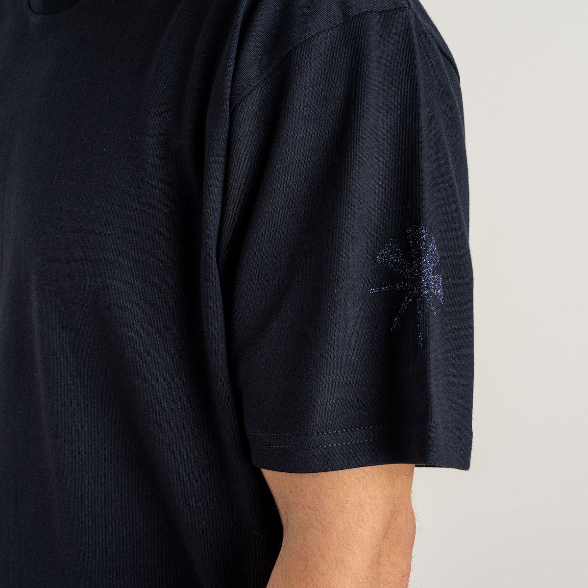 Close-up of two dark blue water signs embroidered near the hem of the navy Water and the Star T-shirt.