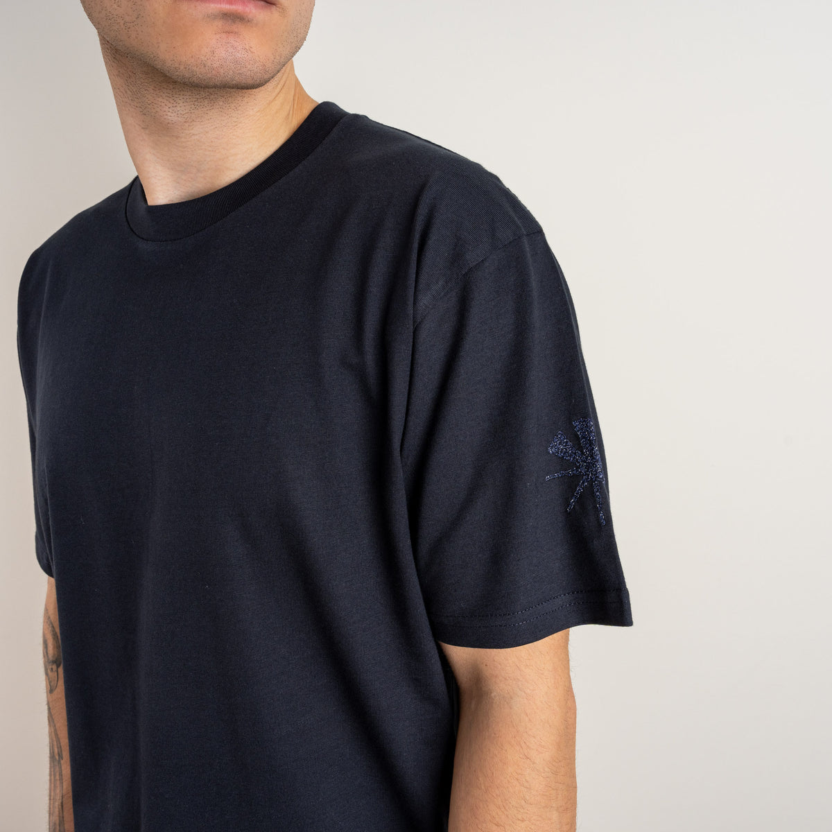 Detailed view of the cuneiform-inspired star stitched on the sleeve of the Gordina navy T-shirt.